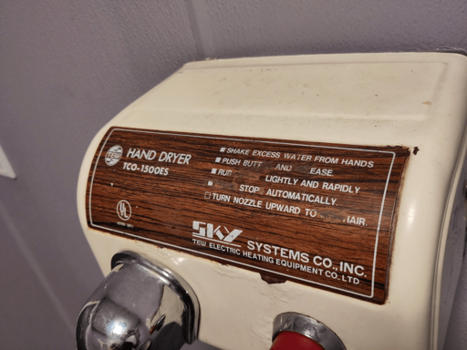 Beige Hand dryer with a wood-pattern plaque, stating comapny name and instructions for use. Some letters and words have been scratched out.

"HAND DRYER
TCO-1500ES
- SHAKE EXCESS WATER FROM HANDS
- PUSH BUTT## AND ##EASE
- RUB #####  LIGHTLY AND RAPIDLY
- ##### STOP# AUTOMATICALLY.
- TURN NOZZLE UPWARD TO ### #AIR.

SKY SYSTEMS CO., INC.
Tew ELECTRIC HEATING EQUIPMENT CO., LTD"